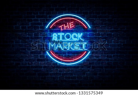 A neon sign in blue and red light on a brick wall background that reads: THE STOCK MARKET