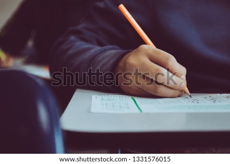 high school or university student holding pencil writing on paper answer sheet.sitting on lecture chair taking final exam attending in examination room or classroom.student in uniform