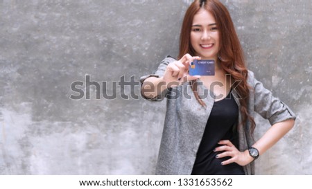 Smiling young woman holding a credit card looking to camera on gray background. Attractive business woman get satisfy and happy with freedom of payment. 