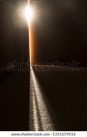 Streaming light coming through a crack in a slightly open door at the end of a dark hallway representing hope and opportunity just beyond the door. Royalty-Free Stock Photo #1331659016