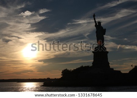 Silhouette of the Statue of Liberty in the sunset with sky, sun and clouds as backdrop 