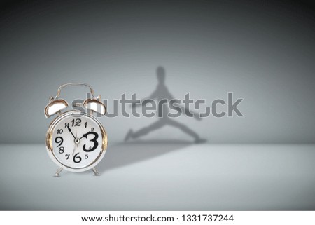 Time Management Concept : Silver alarm clock place on floor and shadow shading reflect on wall in figure running shape.