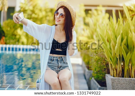 brunette girl using her phone while relaxing by the pool