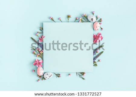 Easter composition. Easter eggs, flowers, paper blank on pastel blue background. Flat lay, top view, copy space. Royalty-Free Stock Photo #1331772527