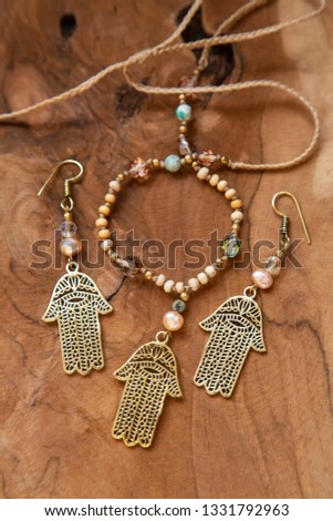 Jewelry set with Hamsa Fatima hand symbol and stone beads on wooden background, blur