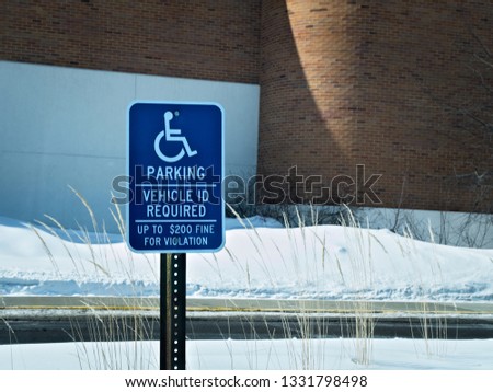 Handicapped parking sign posted in snow covered parking lot in winter.