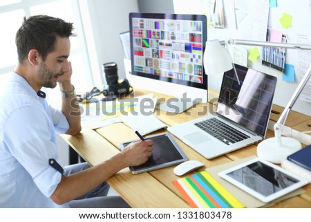 Portrait of young designer sitting at graphic studio in front of laptop and computer while working online.