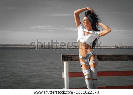 Beautiful portrait of a girl in a short tank top and blue ripped jeans  close-up, rest on the sea or ocean.  Happiness Young woman on the beach at sunset times 