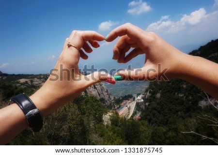 Two female hands make a heart sign. In the background are the Pyrenees Mountains, Catalonia, Spain.