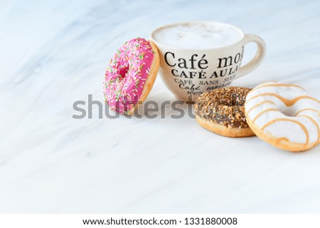 a large Cup of cappuccino coffee and colorful donuts, on the Cup inscription in French (mocha coffee, coffee with milk). pink background, selective focus, without logo