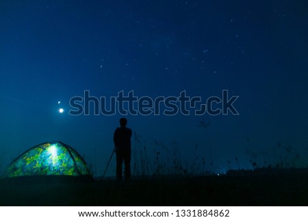 Silhouette tourist standing and take a photo the sky and star in the mid night time.Traveler with camera near the glowing camping tent in the night under a starry sky.