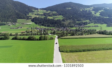 Aerial picture of car driving past camera moving over rural road located in Zillertal valley in background showing Imming village and the Bruckerberg mountain part of the Alps