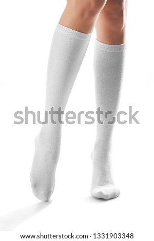 Cropped front shot of woman's slender legs wearing snowy knee high socks. The girl is making a step against the white background. Comfortable legwear for ladies and girls. Stylish women's hosiery. Royalty-Free Stock Photo #1331903348