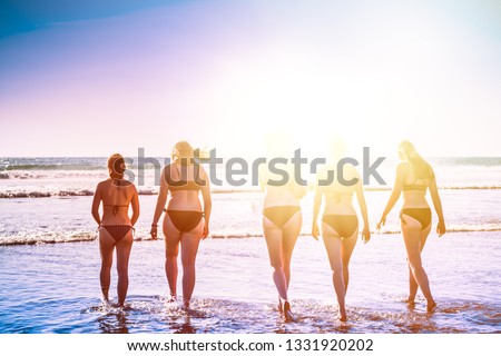 A group of young women splash water as they enter the sea at the beach on a beautiful summer afternoon