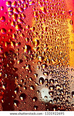 A close-up of droplets of water, rain or condensation on a sheet of transparent material beyond can be seen bright coloured neon colours such as a city street after the rain
