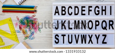 Back to school concept. Letters from A to Z. English alphabet on modern board and accessories for study over white wooden surface, overhead view. From above, flat lay.