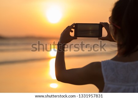 Young woman taking picture of sea sunset