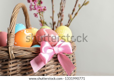Wicker basket with painted Easter eggs and flowers on color background, closeup