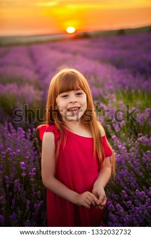 Little girl with blond hair and white dress is holding analog camera in a lavender field