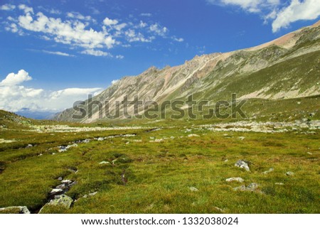 green alpine meadow with hillsides and blue sky with clouds in Teberda, Karachay-Cherkess Republic