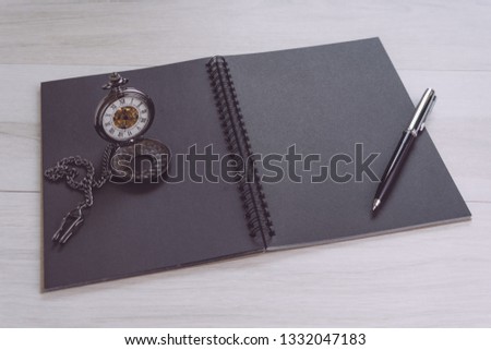 Blank empty black page note book opening with pen and vintage pocket watch on gray wooden table using as time, journal thinking, writing and creativity.