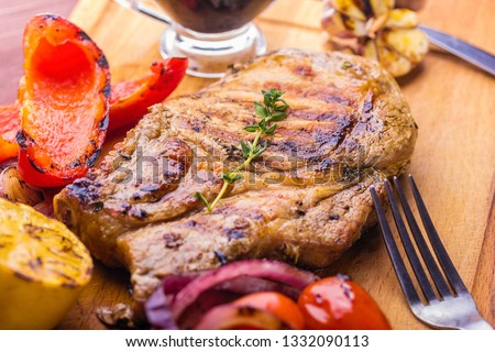 Juicy pork steak with a sprig of fresh thyme, lemon and grilled vegetables close-up. Royalty-Free Stock Photo #1332090113