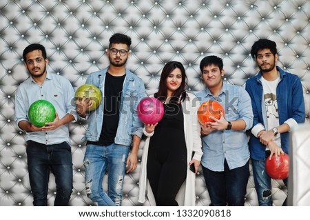 Group of five south asian peoples having rest and fun at bowling club, posing against silver wall with balls at hands.