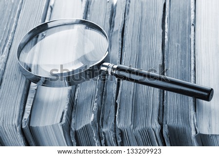 Magnifying glass over the stack of books in grey light