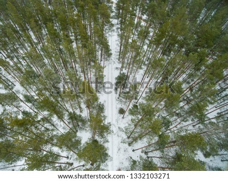 Winter landscape on road in a green forest. Drone view photo on a cloudy day. Aerial top view beautiful snowy landscape.