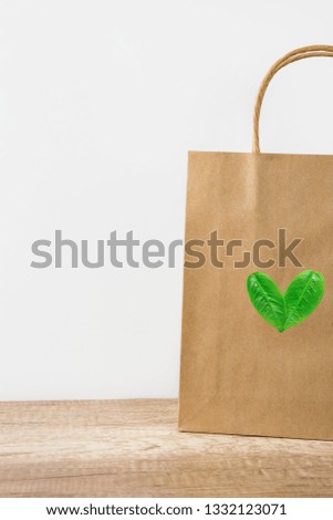 Blank brown craft paper bag on white wall background. Heart logo from leaves. Nature friendly style. Environmental conservation recycling plastic free concept. Copy space