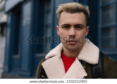 Handsome young man with stylish haircut in trendy casual jacket waiting for taxi outdoor. Portrait of fashion guy posing for pictures outdoor. 
