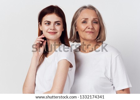 An elderly woman and granddaughter are standing side by side on a gray background in white T-shirts Family