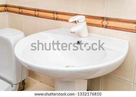 The bright photo of a  white clean sink in a bathroom with metallic tap