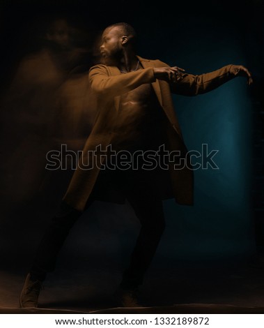 Full length portrait of dancing shirtless man in brown coat and jeans. Studio shot, motion, long exposure