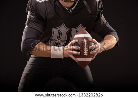 American Football Ball in hands of player on black background