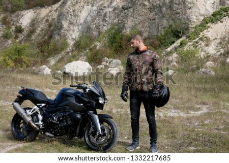 Journey to a motorcycle through a career. A motorcyclist with a helmet in his hands looks at a motorcycle