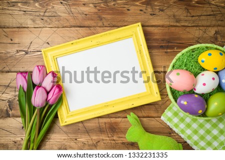 Easter holiday background with photo frame; easter eggs in basket and tulip flowers on wooden table. Top view from above