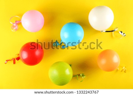 Minimal style composition with different pastel color air balloons with streamer ribbons on bright yellow paper background with a lot of copy space for text. Top view, close up, flat lay.