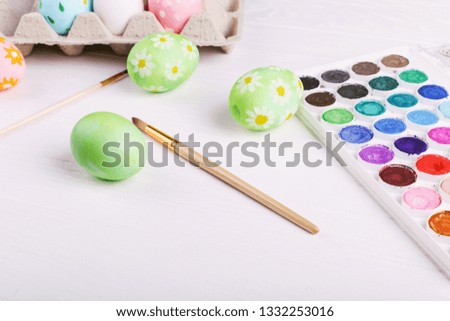 Hand painted Easter eggs, paints and brushes on white table. Preparation for the holiday.