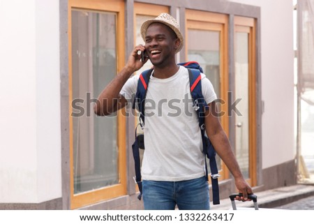 Portrait of happy african american tourist walking with mobile phone and bags through city