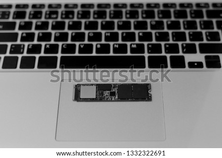 SSD drive chip on the bottom of the laptop. Horizontally on the trackpad. The bottom buttons are not marked, except for the arrow. Black and white photo.