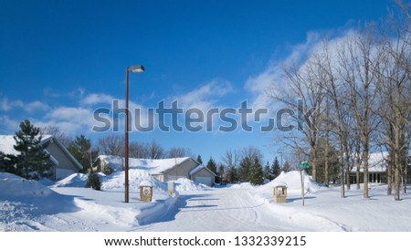 Snow piles along street with houses in Minnesota residential community after winter storms with blue sky and a few clouds.