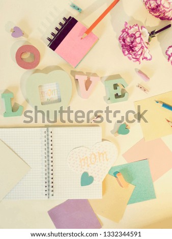 Decorative composition for congratulations on Mother's Day from fresh pink carnations, the volumetric letters, hearts, empty notebooks, crayons, paper, pencils on a light background, top view