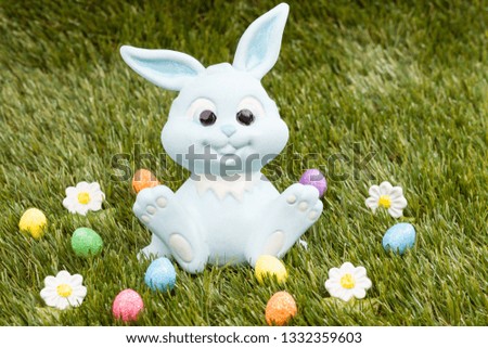 Easter bunny sitting on grass surrounded by colourful easter eggs