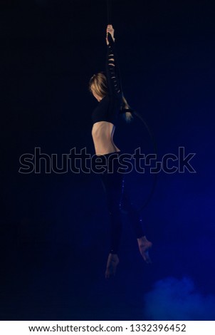 gymnast girl aerial acrobatics on the ring on the background of blue smoke in the dark