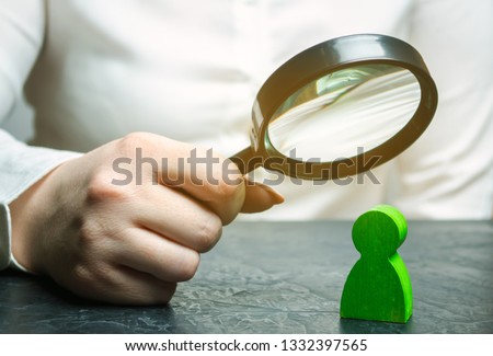 Businesswoman is holding a magnifying glass over a green man figure. Search for a talented employee. Identifying strengths in the company. Disclosure skills. Employee characteristics Royalty-Free Stock Photo #1332397565