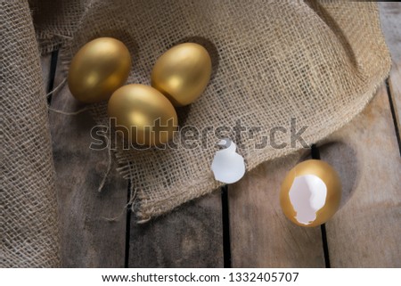 Small group of the golden eggs in birds nest over rustic wooden background and two empty broken golden eggs. Success Symbol or Happy Easter Concept.