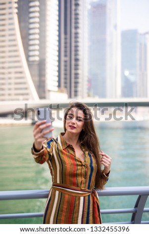 Young woman tourist laughing and taking selfie photo in Dubai Marina in United Arab Emirates. Female traveler and photographer takes picture for her blog.Young happy tourist making selfie
