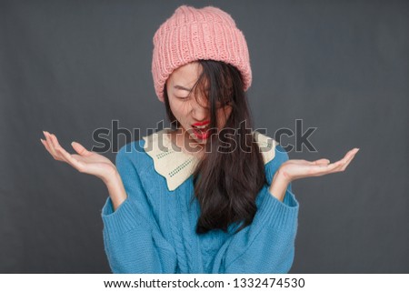 A beautiful Korean girl in a blue sweater and pink hat is wriggling in front of the camera. studio photo shoot, girl posing.