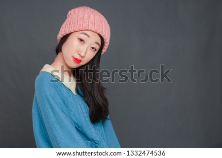 A beautiful Korean girl in a blue sweater and pink hat is wriggling in front of the camera. studio photo shoot, girl posing.